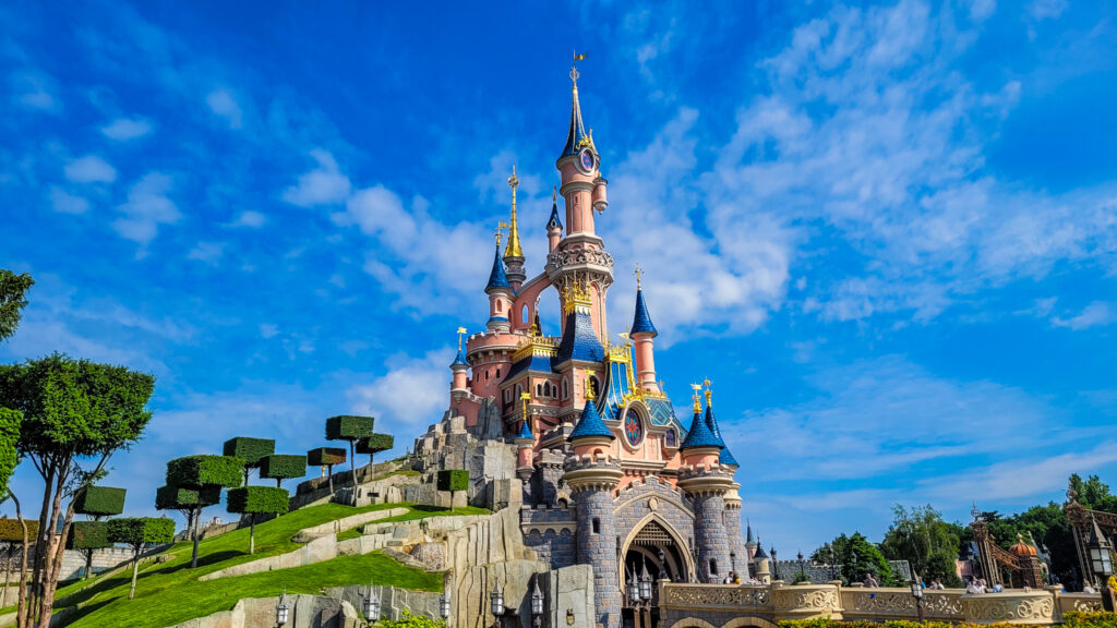 Ein rosafarbenes Märchenschloss mit blauen Dächern vor einem blauen Himmel: das Dornröschenschloss in Disneyland Paris.